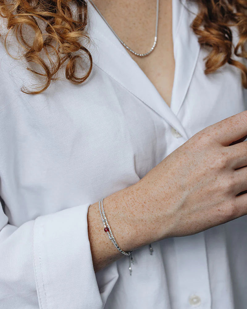 Auf dem Bild sieht den Oberkörper einer Frau mit roten Locken und einer weißen Bluse. Sie trägt eine Kette mit silbernen Perlen und das dazugehörige Armband. Dazu trägt sie ein weiteres Armband aus Perlen und einer Glasperle in Beere.