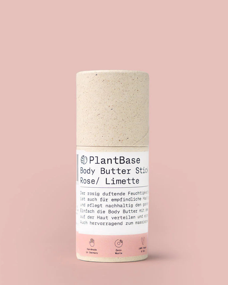 Der Hintergrund ist rosa. Das Produkt (der Body Butter Stick Rose / Limette) ist ein Zylinderförmiger Stick aus Graspapier mit einer Banderole, die weiß/rosa ist und auf der die Infos zum Produkt stehen.