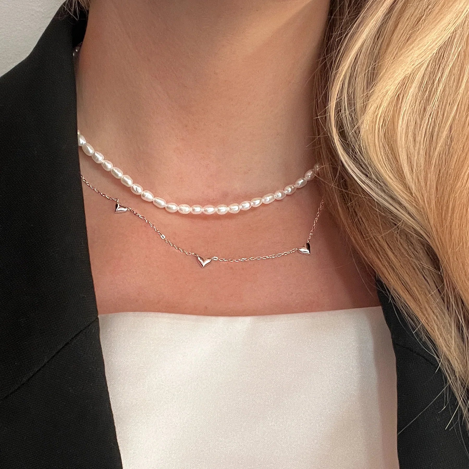 Dekolletee einer Frau mit einer Süßwasserperlen Kette und einer nachhaltigen Kette mit kleinen Herzen aus Silber und Weißgold.
