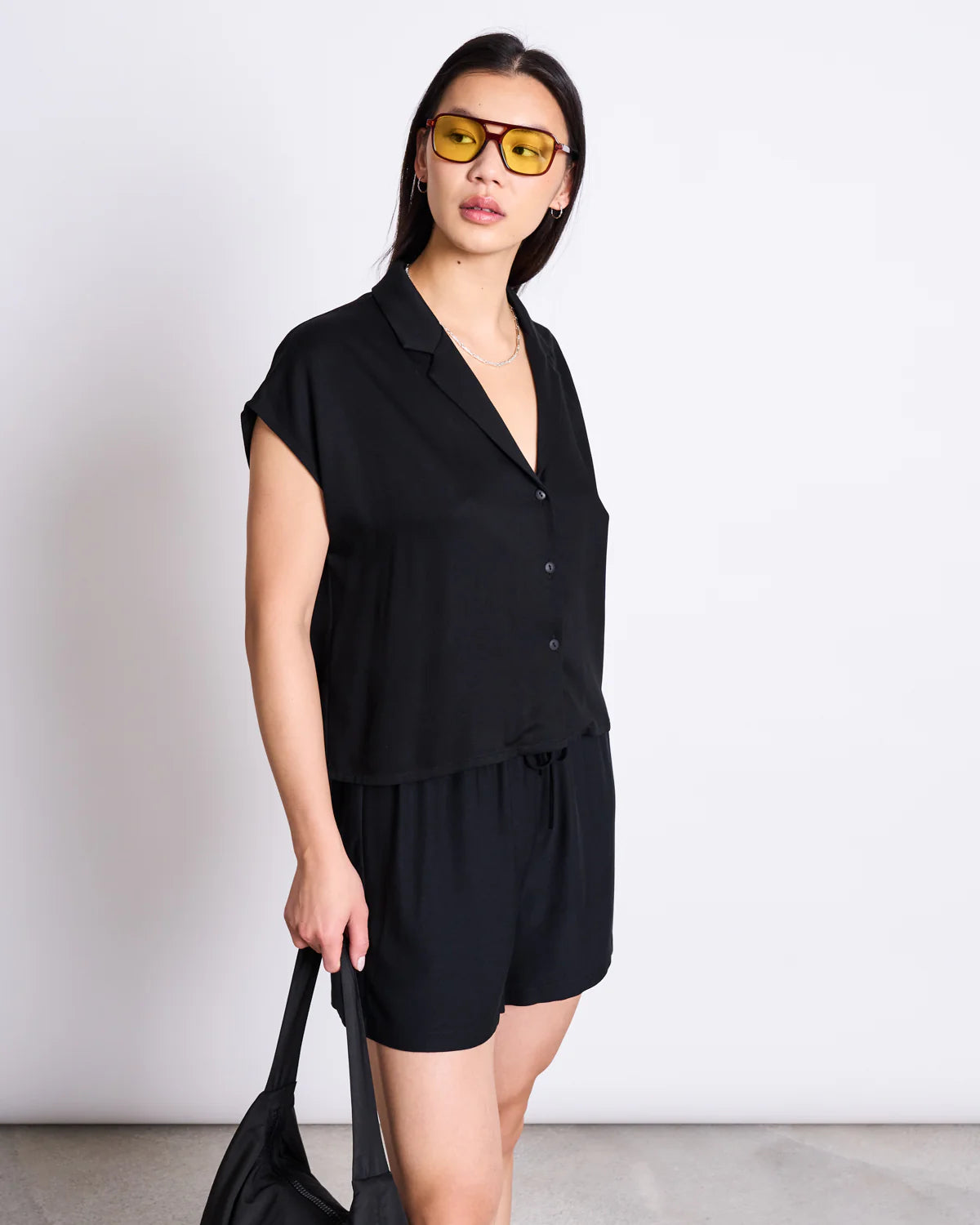 Frau von vorne trägt nachhaltige schwarze Bluse mit Knopfleiste und Reverskragen und fair produzierte schwarze Shorts.