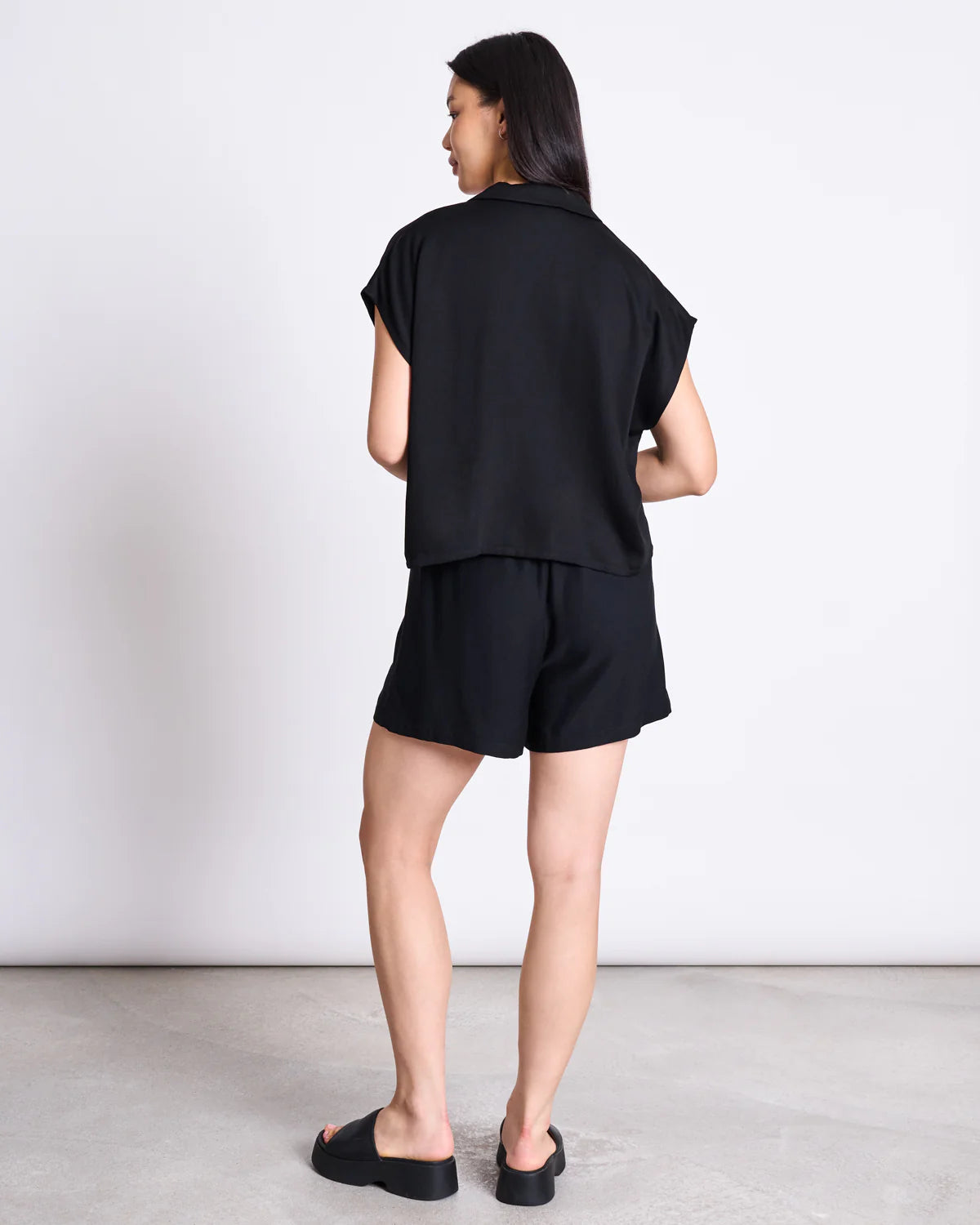 Frau von hinten trägt nachhaltige schwarze Bluse und fair produzierte Shorts.
