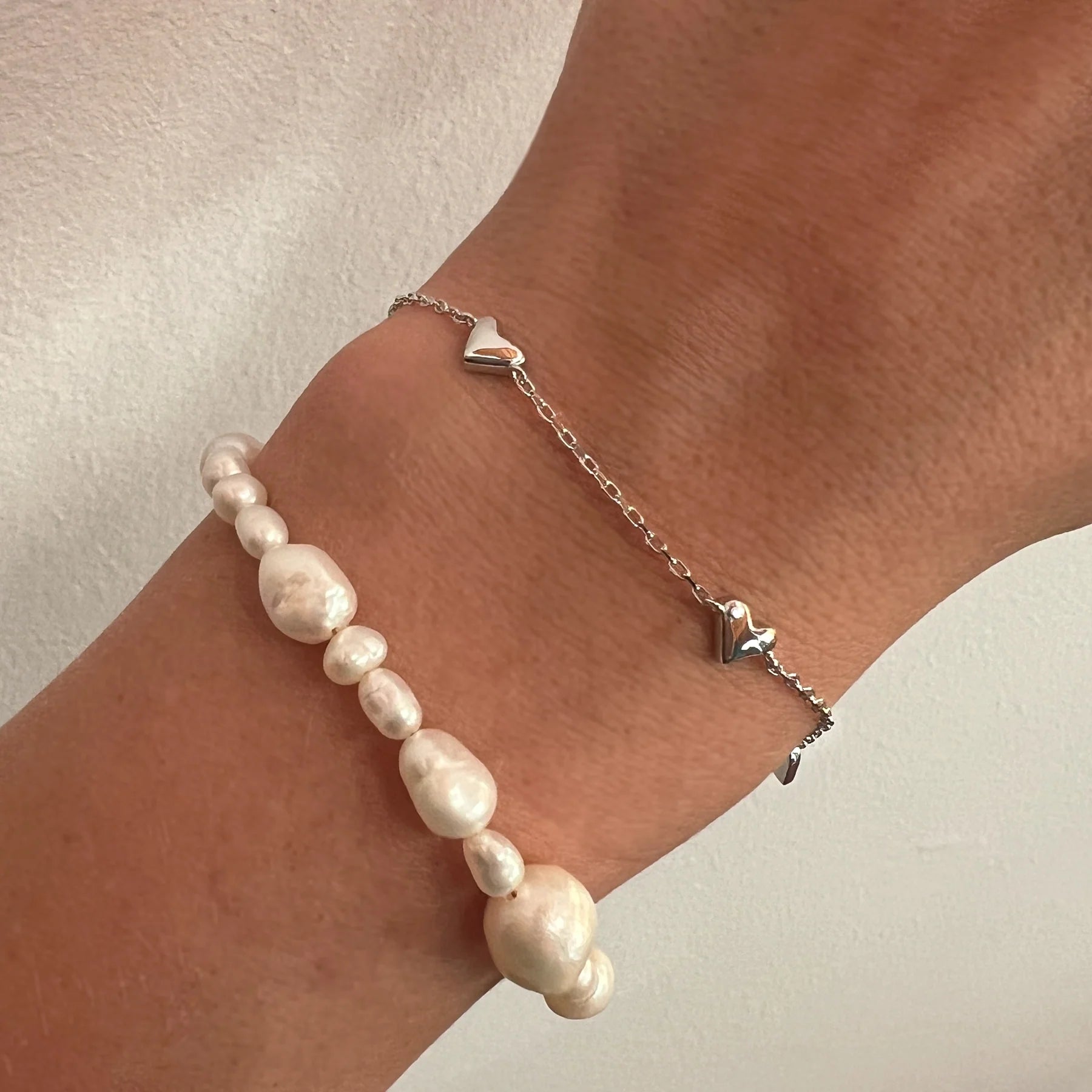 Handgelenk mit nachhaltigen Süßwasserperlen Armband und fair produziertem Armband mit kleinen Herzen aus Silber und Weißgold. 