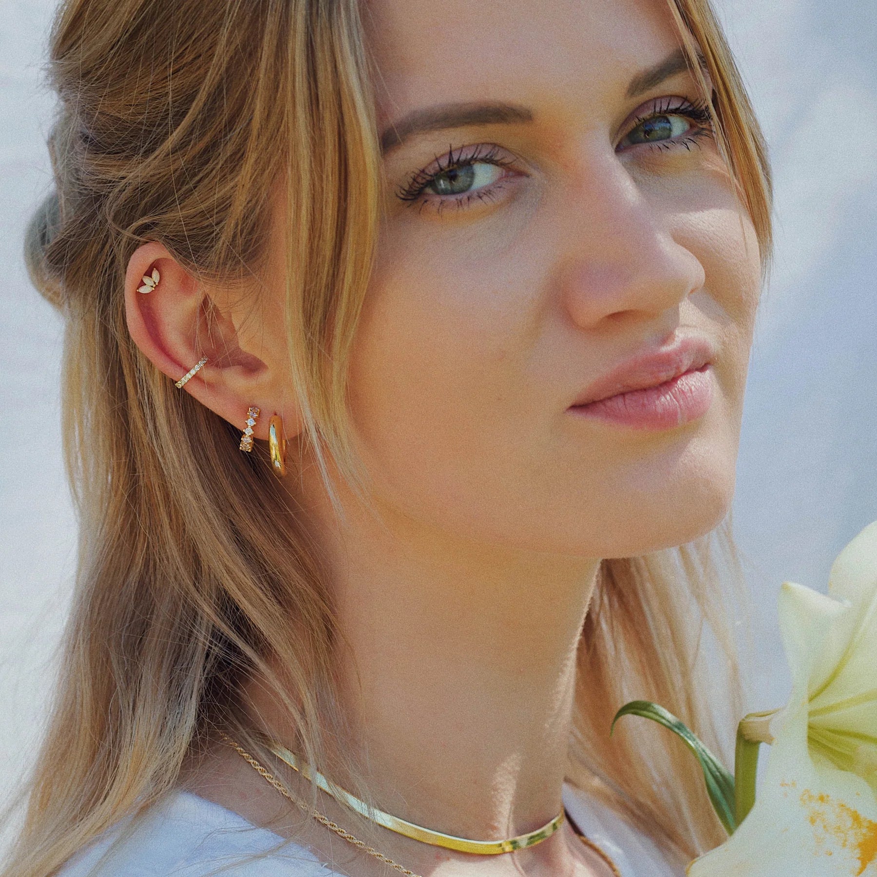 Nahaufnahme einer Frau mit fair produzierten goldenen Creolen, einem funkelnden Earcuff und einem Helix Ohrstecker in Gold. 