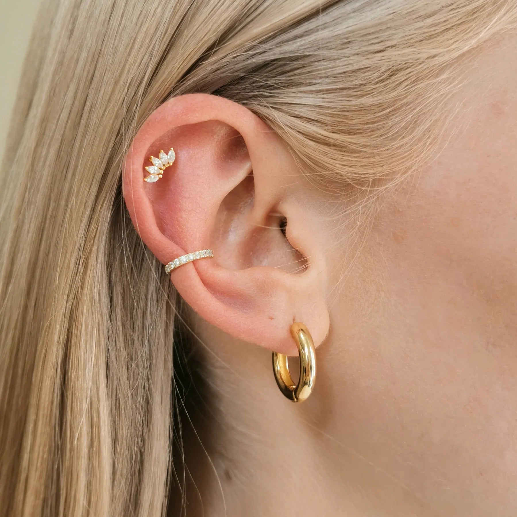 Nahaufnahme eines Ohrs mit fair produzierten goldenen Creolen, einem funkelnden Earcuff und einem Helix Ohrstecker in Gold. 