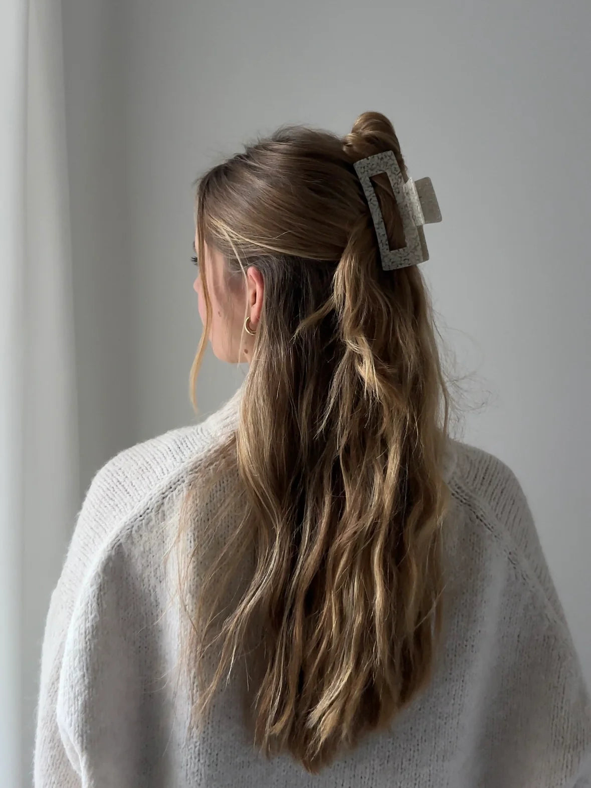 Frau von hinten in einem hellen Pullover, die ihre Haare mit einer großen Haarklammer in cremeweiß gesprenkelt aus cellulose acetat zusammengesteckt hat.