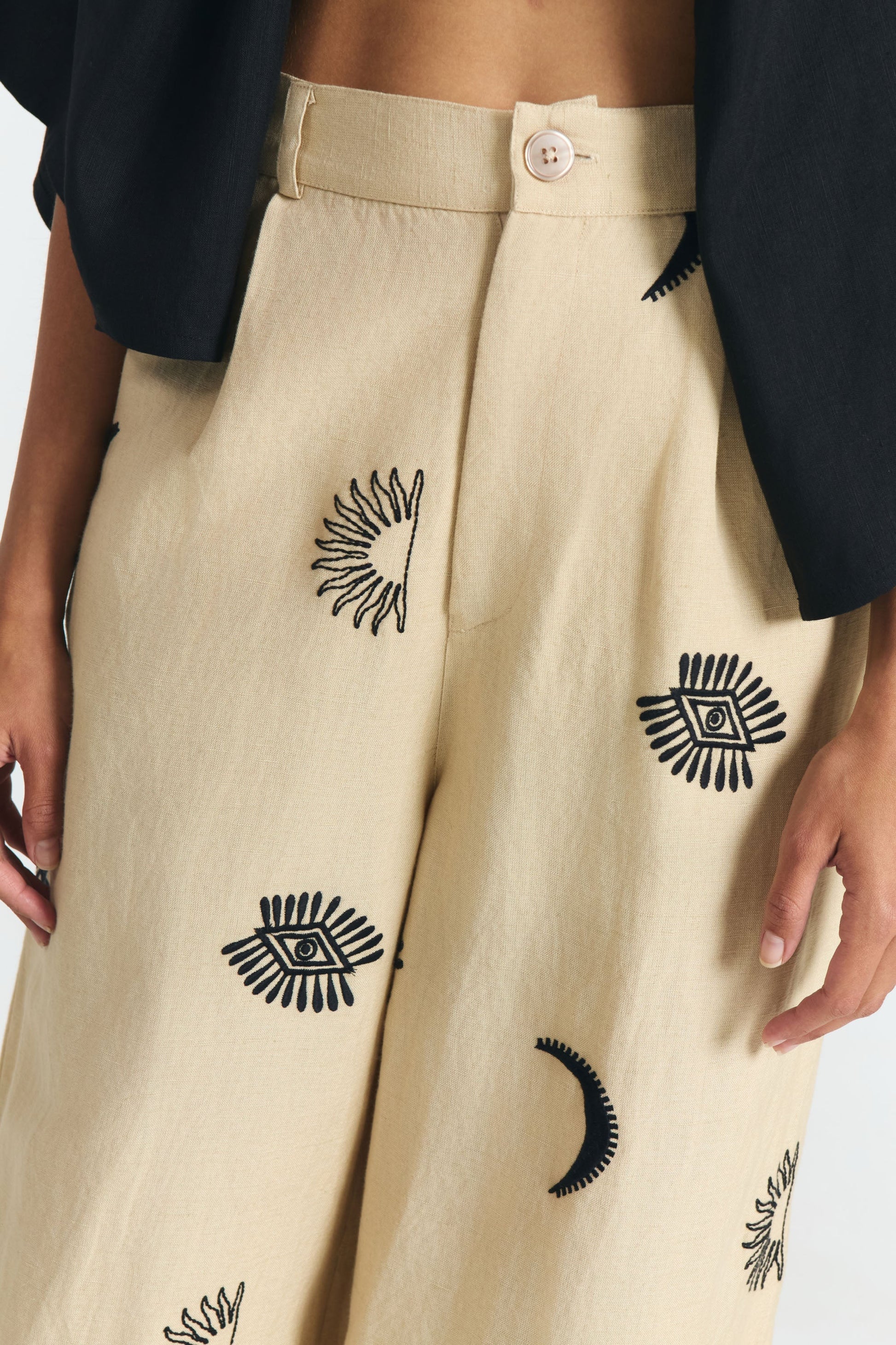 Nahaufnahme der fair produzierten weiten Hose in beige mit Stickereien aus Mond, Sonne, Augen.